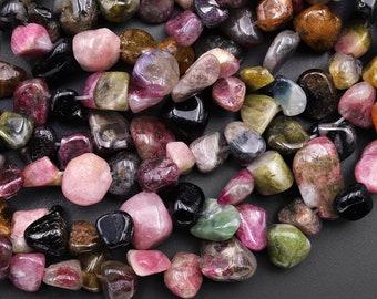 May include: A collection of tumbled multi-colored gemstones, including pink, green, black, and brown. The stones are smooth and polished, and they are arranged in a random pattern.