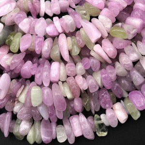 Pode incluir: Close-up de uma coleção de pedras preciosas polidas em tons de rosa, lavanda e verde pálido. As pedras têm formato e tamanho irregulares, com acabamento polido e brilhante. Ideal para a criação de joias.