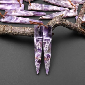 May include: A pair of amethyst earrings with a pointed, teardrop shape. The earrings have a purple and white banded pattern.