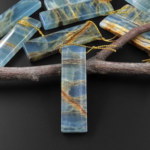 Puede incluir: Una colección de colgantes de ágata rayados azules y marrones con un cordón dorado atado. Los colgantes están dispuestos en una rama.