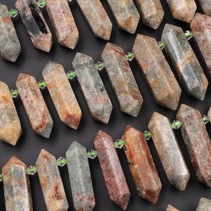 May include: A collection of green, brown, and red gemstone points with a clear crystal bead on each point. The points are arranged in rows on a dark surface.
