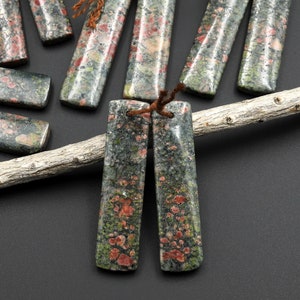 May include: A pair of long, rectangular, green and red gemstone earrings with a speckled pattern. The earrings are tied together with brown string.