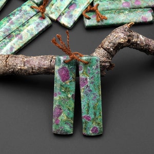 Könnte beinhalten: Zwei rechteckige Ohrringe aus grünem und rosafarbenem Edelstein mit braunen Schnüren.