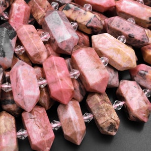 Puede incluir: Primer plano de un montón de cuentas de piedras preciosas rosas y marrones. Las cuentas son facetadas y tienen una textura natural y rugosa. Están enhebradas en un cordón transparente con detalles plateados.