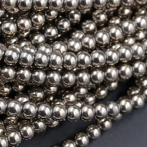 May include: A strand of silver-toned round beads. The beads are smooth and shiny, and they are arranged in a pile.