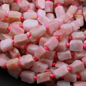 May include: A strand of pink opal beads, each bead is a rectangular shape with a slightly irregular, natural finish. The beads are strung on a pink thread.