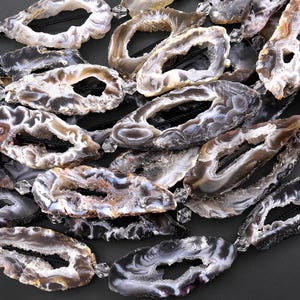 May include: A collection of agate slices with natural holes, featuring a variety of gray, white, and brown tones. The slices are strung together with black cord and have a polished finish.
