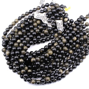 May include: A strand of black and gold obsidian beads. The beads are round and have a smooth, polished finish. The beads are strung on a clear elastic cord.