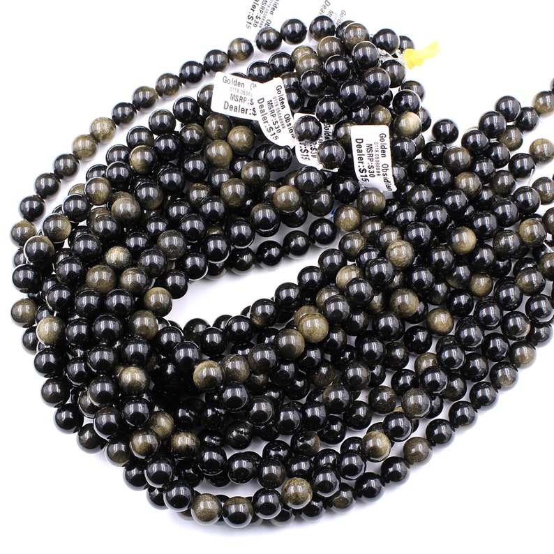 May include: A strand of black and gold obsidian beads. The beads are round and have a smooth, polished finish. The beads are strung on a clear elastic cord.