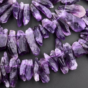 May include: Raw amethyst crystal beads in varying sizes and shapes. The crystals are a deep purple color with natural facets and textures. The beads are strung together, ready for jewelry making or other crafts.