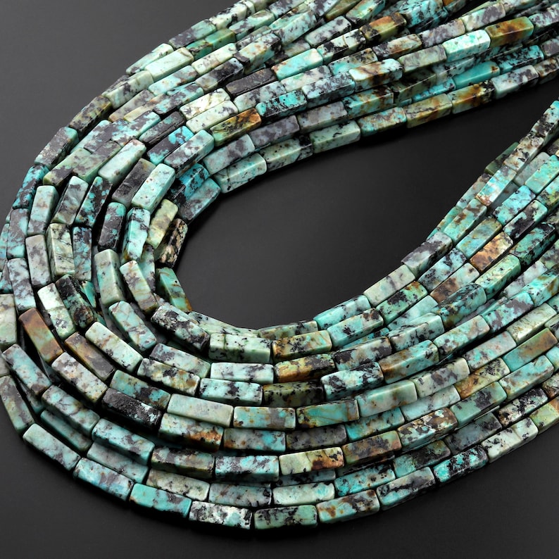 May include: A strand of turquoise gemstone beads, each bead is a rectangular shape with a mottled green, blue, and brown pattern.