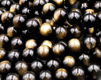 May include: A close-up of a pile of black and gold beads. The beads are round and have a smooth, polished finish. The gold color is a subtle shimmer that adds a touch of elegance to the beads.