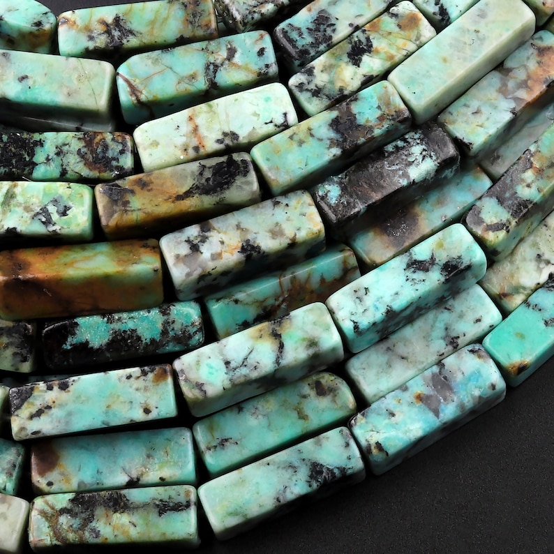 May include: A strand of turquoise gemstone beads, each bead is a rectangular shape with a mottled green, blue, and brown pattern.