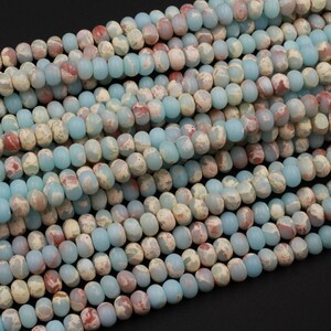 May include: Strands of gemstone beads in shades of pale blue, cream, and reddish-brown. The beads are oval-shaped and have a slightly matte finish. The beads are strung together, creating a textured and colorful pattern. Ideal for jewelry making.