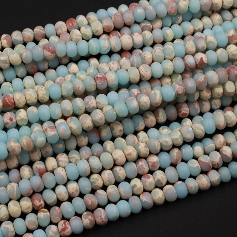 May include: Strands of gemstone beads in shades of pale blue, cream, and reddish-brown. The beads are oval-shaped and have a slightly matte finish. The beads are strung together, creating a textured and colorful pattern. Ideal for jewelry making.