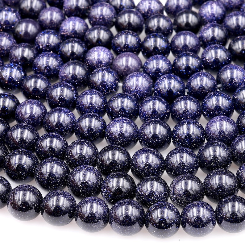 Op de afbeelding: Een streng donkerblauwe edelsteen kralen met een gespikkelde, glinsterende afwerking. De kralen zijn rond en glad en zijn geregen op een doorzichtige draad.