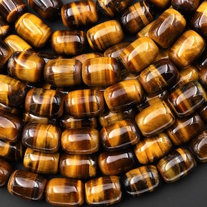 May include: Close-up of a collection of polished tiger eye gemstone beads. The beads are a mix of golden brown and dark brown, with a chatoyant effect. The beads are oval-shaped and have a smooth, glossy finish. Ideal for jewelry making.