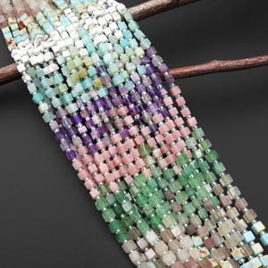 May include: Strands of colorful gemstone beads in various shades of pink, green, purple, and blue. The beads are square-shaped and strung together with silver-colored metal. The gemstones are arranged in a gradient pattern.