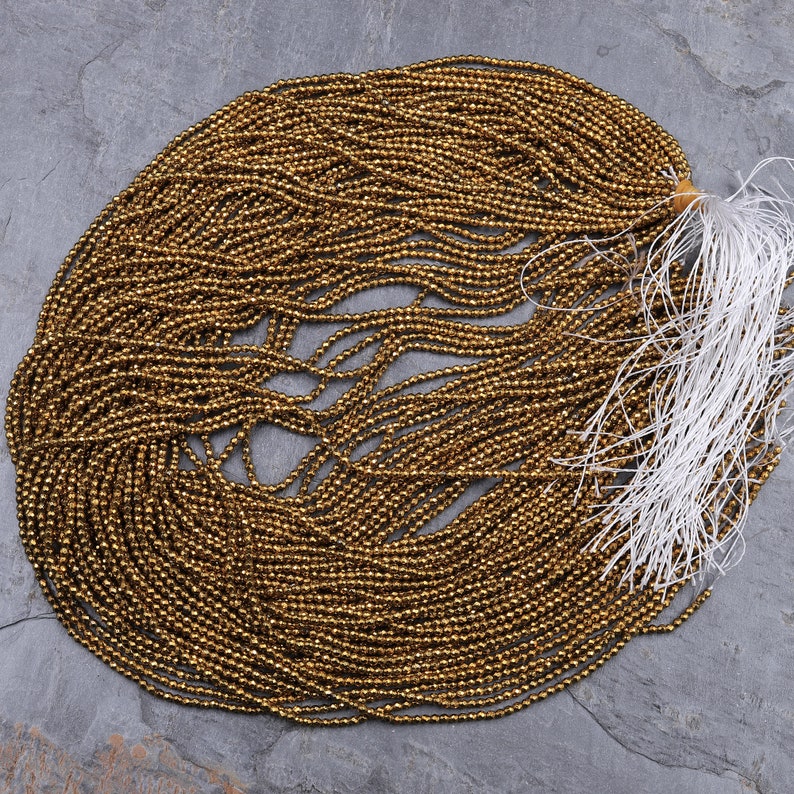 May include: A large quantity of small, round, gold-colored beads. The beads are arranged in a circular pattern and have a shiny, metallic finish.