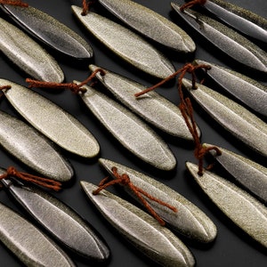 May include: A collection of gold and brown, long, oval-shaped beads with a shimmery, textured surface. Each bead has a brown string tied around it.