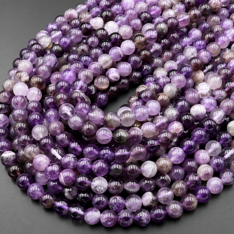 May include: A strand of round, purple amethyst beads. The beads are smooth and have a slight shine. The beads are all approximately the same size.
