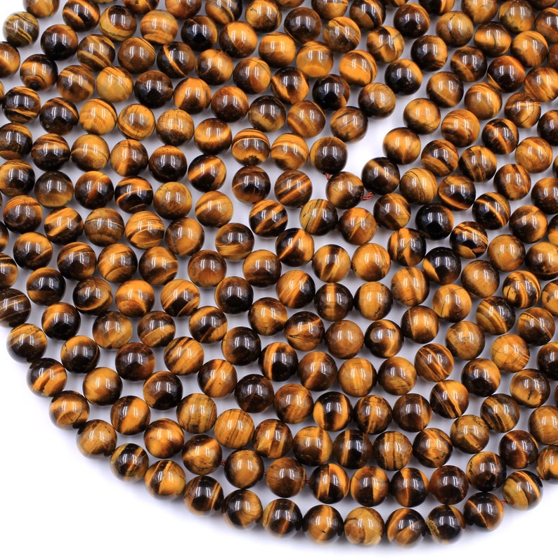 May include: A strand of round, polished tiger's eye beads. The beads are a mix of golden brown and black colors with a shimmering, iridescent effect.