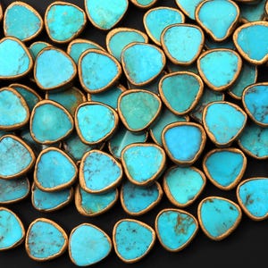 Peut inclure: Gros plan sur une collection de perles de turquoise avec des bords dorés. Les perles sont de forme irrégulière et ont une finition lisse et polie.