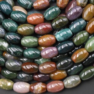 Puede incluir: Un conjunto de cuentas de piedras preciosas pulidas en varios colores, incluyendo verde, naranja, rojo y morado. Las cuentas, de forma ovalada, están ensartadas, mostrando un acabado natural y brillante. Ideal para la creación de joyas.