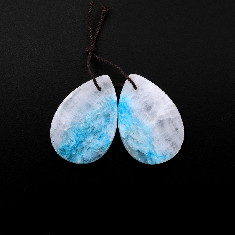 May include: A pair of teardrop-shaped blue and white agate gemstone earrings with brown string ties.