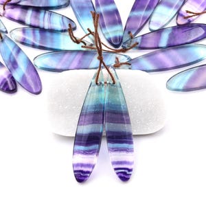 May include: Two long, teardrop-shaped, purple and blue fluorite gemstone pendants with brown leather cord.