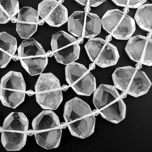 May include: A strand of clear quartz crystal beads, each bead is faceted and has a unique shape. The beads are strung on a white thread.