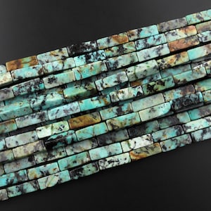 May include: A strand of turquoise gemstone beads, each bead is a rectangular shape with a mottled pattern of blue, green, brown, and black.