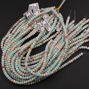 May include: Strands of Impression Jasper beads in shades of pale blue, cream, and reddish-brown. The beads are small, round, and strung together, with price tags attached. The beads are a natural stone material.