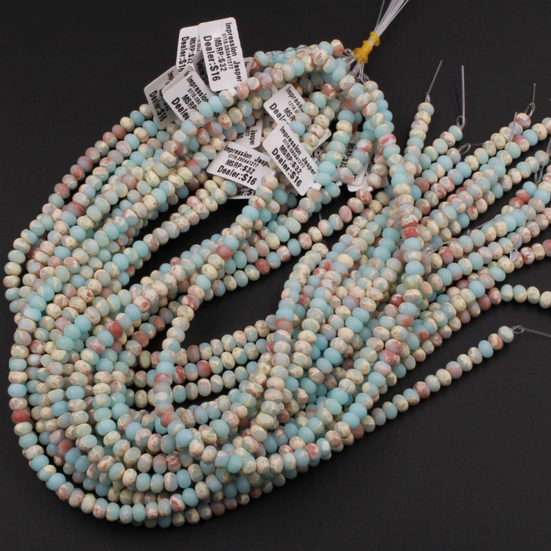 May include: Strands of Impression Jasper beads in shades of pale blue, cream, and reddish-brown. The beads are small, round, and strung together, with price tags attached. The beads are a natural stone material.