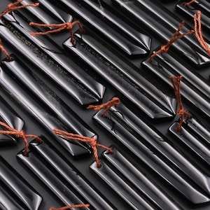 May include: A collection of black obsidian arrowheads with brown string tied around the top. The arrowheads are arranged in a diagonal pattern.