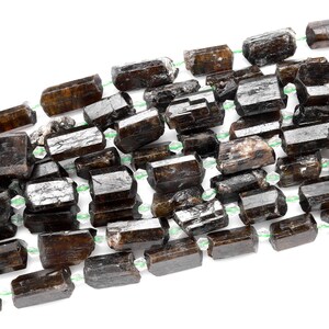 Puede incluir: Una hebra de cuentas de piedras preciosas de color marr&oacute;n oscuro, facetadas y alargadas. Las cuentas est&aacute;n enhebradas en un hilo transparente con peque&ntilde;as cuentas espaciadoras verdes.
