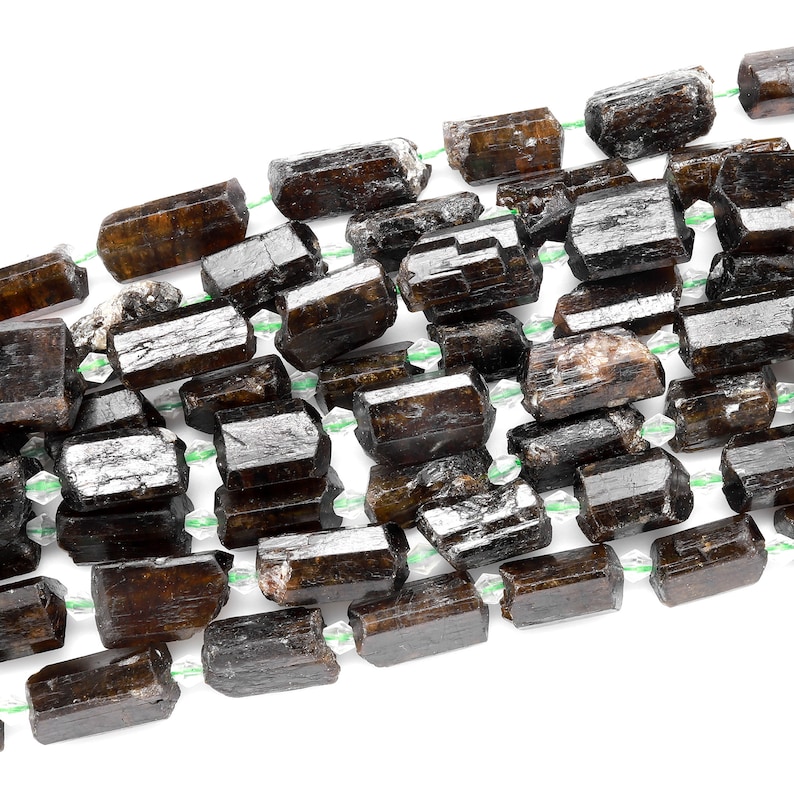 Puede incluir: Una hebra de cuentas de piedras preciosas de color marr&oacute;n oscuro, facetadas y alargadas. Las cuentas est&aacute;n enhebradas en un hilo transparente con peque&ntilde;as cuentas espaciadoras verdes.