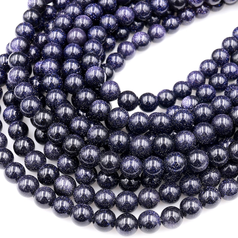 Op de afbeelding: Een streng donkerblauwe edelsteen kralen met een gespikkelde, glinsterende afwerking. De kralen zijn rond en glad en zijn gerangschikt in een cirkelvormig patroon.