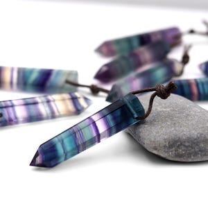 May include: A collection of rainbow fluorite crystal points with brown leather cords. The crystals are a mix of purple, blue, green, and white.