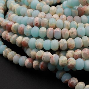 May include: Strands of gemstone beads in shades of pale blue, cream, and reddish-brown. The beads are oval-shaped and have a matte finish. The beads are strung together, creating a textured and colorful pattern. Ideal for jewelry making.