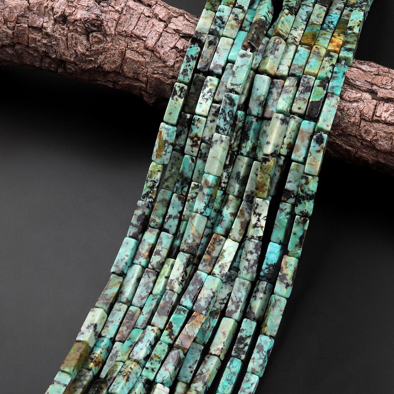 May include: A strand of turquoise gemstone beads, each bead is a rectangular shape with a mottled green and brown pattern.