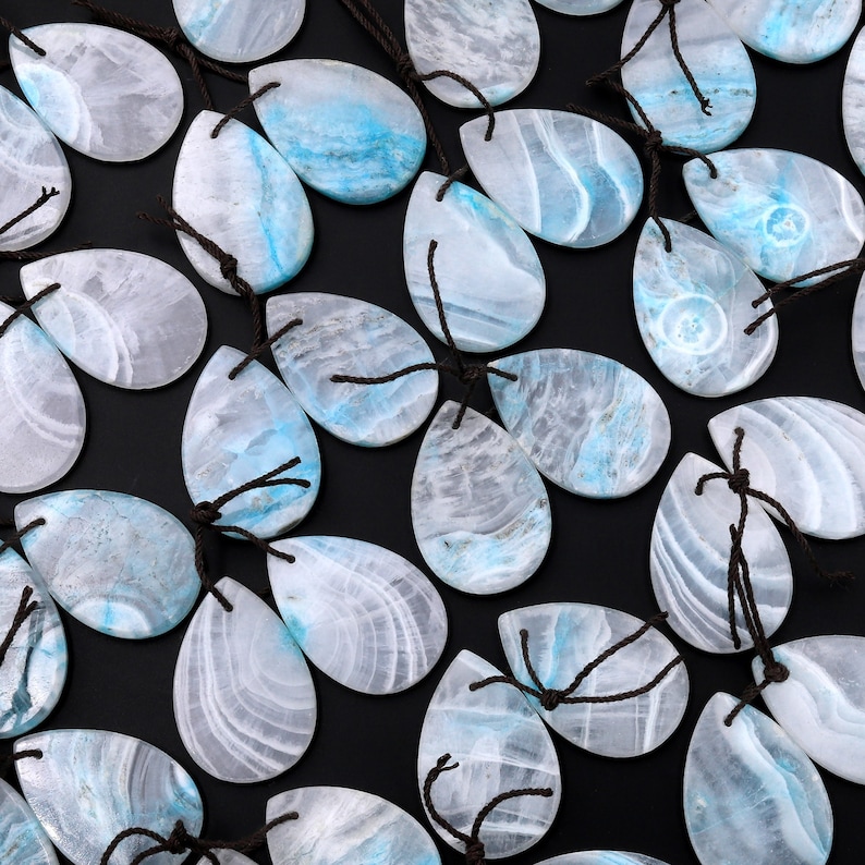 May include: A collection of teardrop-shaped blue and white gemstone pendants with brown string attached. The stones have a swirling pattern of blue and white.