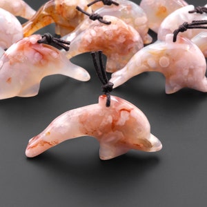 May include: A group of carved agate dolphin pendants with brown cords. The dolphins are a light pink color with white and brown markings.