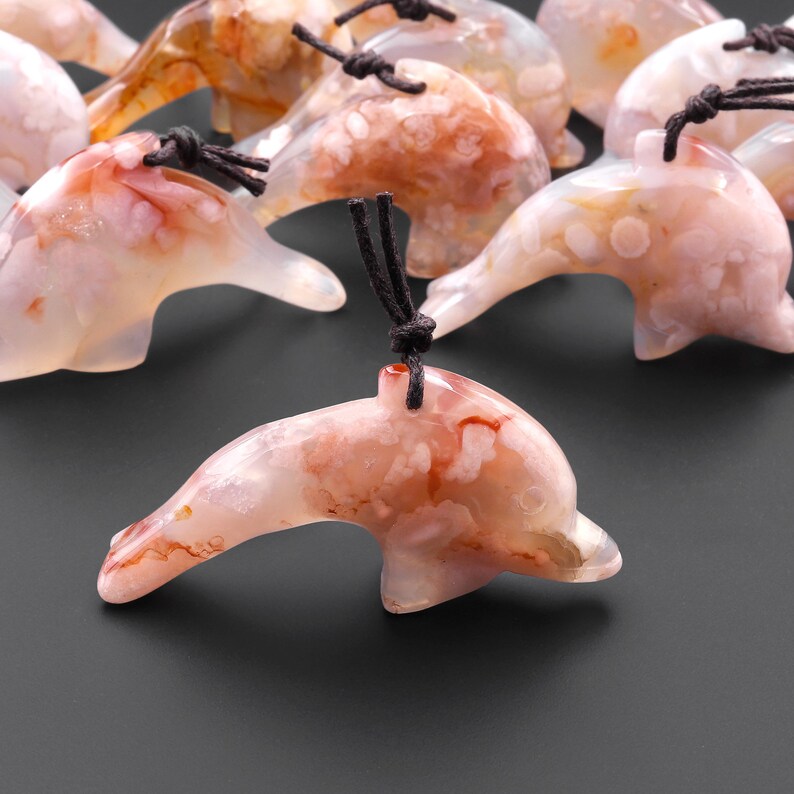May include: A group of carved agate dolphin pendants with brown cords. The dolphins are a light pink color with white and brown markings.
