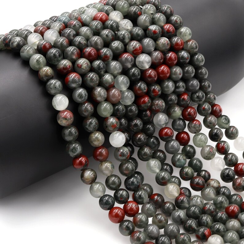 May include: A strand of round, green, red, and white gemstone beads. The beads are approximately 6mm in diameter and have a speckled, marbled appearance.