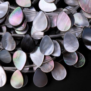 May include: A strand of iridescent teardrop-shaped beads in shades of black, white, and gray. The beads are made of mother-of-pearl and have a smooth, polished finish.