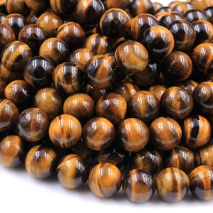 May include: A close-up of a pile of round, polished tiger's eye beads. The beads are a mix of golden brown and black colors with a shimmering, iridescent effect.