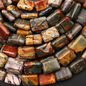 May include: A collection of rectangular polished jasper beads featuring a variety of earthy tones including ochre, rust red, olive green, and cream, with intricate dark brown veining and natural patterns visible across the smooth stone surfaces.