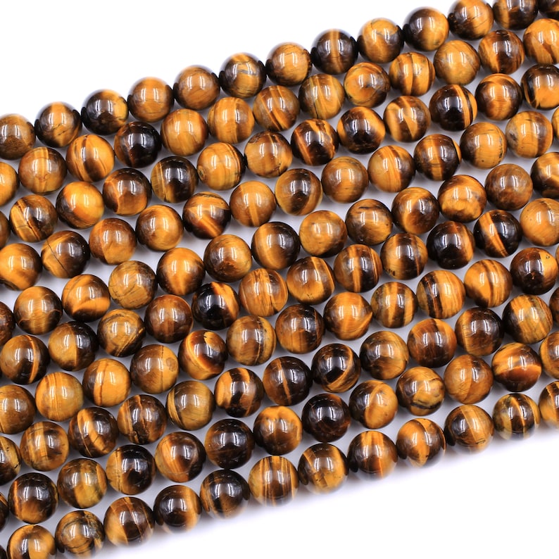 May include: A strand of round, golden brown tiger's eye beads. The beads have a shimmering, chatoyant effect.