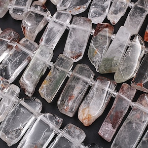 Puede incluir: Una colección de puntas de cristal de cuarzo transparente con inclusiones de verde, marrón y rojo. Las puntas son de varios tamaños y formas, y son perfectas para la elaboración de joyas o la curación con cristales.